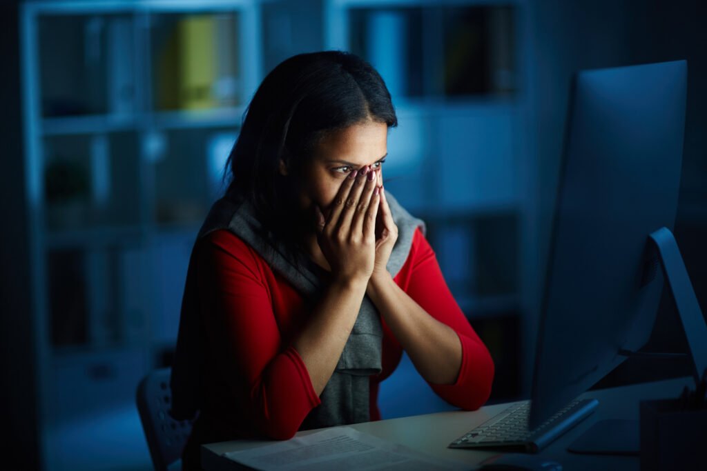 Scared woman covering her face while looking at computer during digital arrest scam.