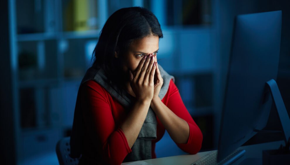 Scared woman covering her face while looking at computer during digital arrest scam.