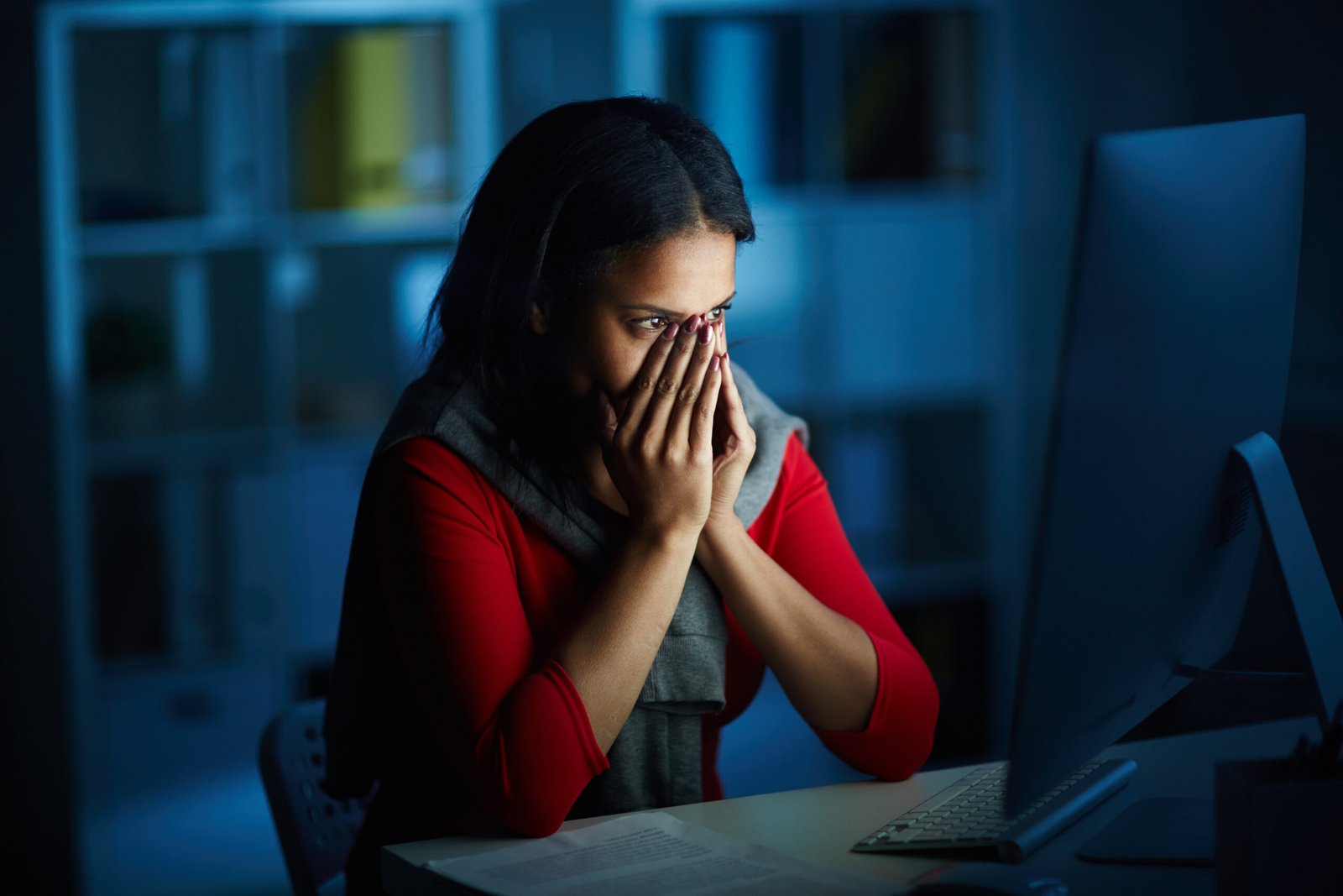 Scared woman covering her face while looking at computer during digital arrest scam.